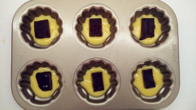 从冰箱中取出面糊，稍微回温之后，将面糊挤入模具中。挤到约三四分满，取出冷冻巧克力块，切成合适大小，将它放在面糊中间。