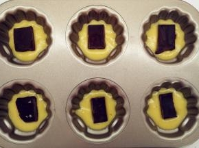 从冰箱中取出面糊，稍微回温之后，将面糊挤入模具中。挤到约三四分满，取出冷冻巧克力块，切成合适大小，将它放在面糊中间。