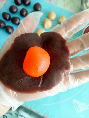 把豆沙按成饺子皮样子，然后放上一颗蛋黄包好待用。