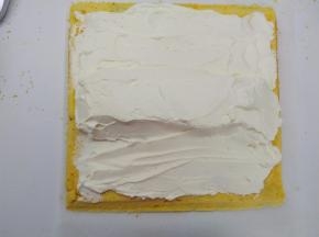 用抹刀在蛋糕体上均匀的抹上一层奶油馅，然后在离自己较近的一侧1/3处用奶油馅堆砌一个小山丘。