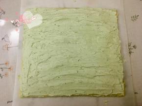 16、蛋糕片盖上油纸，把油纸和蛋糕片翻过来，切去尾端，抹上抹茶淡奶油；