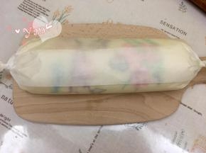 17、用擀面杖卷住油纸，顺势往上推。卷起来，两边跟拧糖一样拧起来。放入冰箱冷藏半小时后再切块食用。