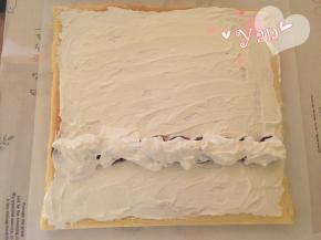 16、蛋糕片盖上油纸，把油纸和蛋糕片翻过来，切去尾端，抹上淡奶油，摆上喜欢的水果，把剩下的淡奶油盖在水果上；