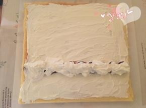 16、蛋糕片盖上油纸，把油纸和蛋糕片翻过来，切去尾端，抹上淡奶油，摆上喜欢的水果，把剩下的淡奶油盖在水果上；