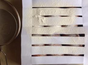 在发酵好的面包坯上铺一张剪好的条纹纸，在上方过筛低粉。