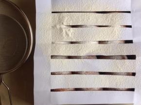 在发酵好的面包坯上铺一张剪好的条纹纸，在上方过筛低粉。