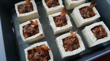 14．豆腐盒中间放调好的馅料，把虾尾插上去装饰，烤盘中加适量高汤。