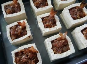 14．豆腐盒中间放调好的馅料，把虾尾插上去装饰，烤盘中加适量高汤。