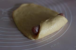 将面团擀成牛舌状，放入香肠，卷起。