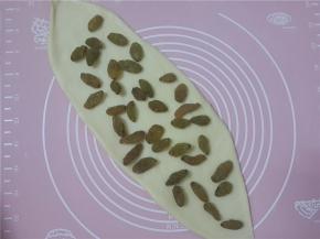 然后擀成椭圆，上面撒入均匀的葡萄干。然后均匀的往里卷起。