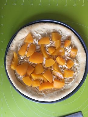 取出烤好的披萨皮，刷一层炼乳，撒上一层马苏里拉芝士碎，然后把黄桃切小块摆入