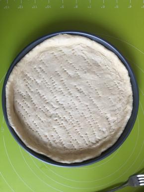 松弛好的面团擀成和9寸披萨盘一样的大小，披萨盘内抹一层橄榄油，放入面皮，用叉子插上小孔