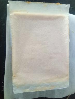 烤好的蛋糕体取出，在桌上轻震一下，倒扣在铺了油纸的烤网上，底下的油纸揭掉，再盖在蛋糕体上，以免蛋糕干掉。