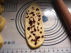 擀开成长舌状，撒上约8克的蔓越莓干，卷起。