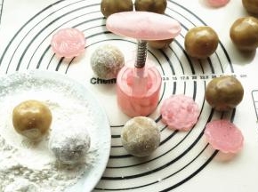 包好的月饼球，在生粉里滚一圈，然后再抖去多余的淀粉，月饼花片也在生粉里滚一下并抖干净粉。