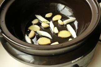 电砂锅底部刷油，铺上姜片、葱段和蒜。