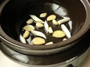 电砂锅底部刷油，铺上姜片、葱段和蒜。