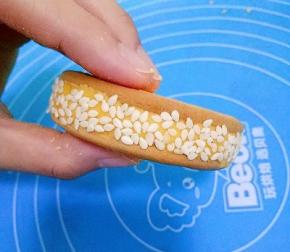 取另一块饼干盖在面团上，将面团夹在中间，形成夹心，然后把饼放在芝麻里滚一圈，让饼周围都均匀的沾上芝麻