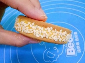 取另一块饼干盖在面团上，将面团夹在中间，形成夹心，然后把饼放在芝麻里滚一圈，让饼周围都均匀的沾上芝麻