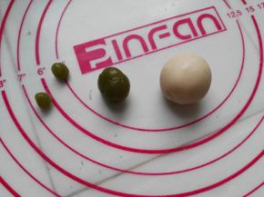 以绿色小企鹅的制作为例，将绿茶桃山皮按5克、0.5克、0.5克的比例分成三等份搓圆，10克牛奶桃山皮搓圆待用
