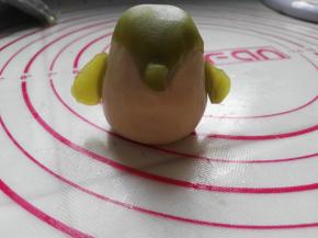 前面捏一下，做个小鼻子，将两个小水滴面团分别按在牛奶桃山皮面团的两侧作为小企鹅的两个小手（见图）