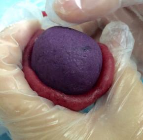 取一个红色的冰皮面团压扁，像包汤圆的手法一样把紫薯包住，搓圆放到模具里轻压在操作台上