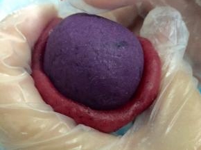 取一个红色的冰皮面团压扁，像包汤圆的手法一样把紫薯包住，搓圆放到模具里轻压在操作台上