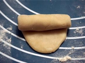案板上洒少许面粉，用面杖将面团擀成椭圆形，由上往下卷起来。