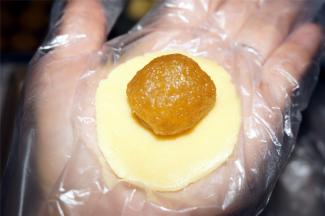 取一块称好的酥皮面团，揉成圆形，用手把面团压扁，放上一块凤梨馅。