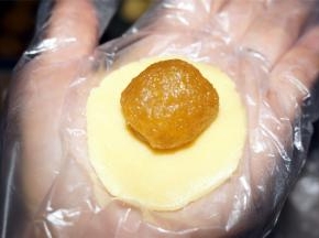 取一块称好的酥皮面团，揉成圆形，用手把面团压扁，放上一块凤梨馅。