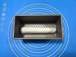 自上向下卷起，收口向下，放入吐司盒中，盖保鲜膜放温暖处进行第二次发酵。