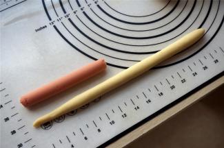 取一份面团，揉光滑后，搓成长条状，长度约为火腿肠的两倍。