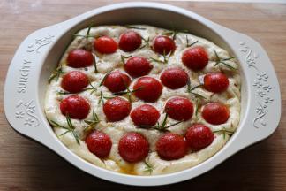 小番茄和迷迭香按压在面团上，撒上适量盐和黑胡椒粉；