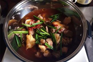 然后放入猪手，淋上南乳汁，放入盐，糖，生抽，老抽，料酒，表面铺上大蒜叶，从四周加入1000毫升清水。