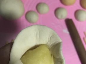 16.取一个白色面团擀薄，包入奶黄馅封口。
