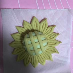 18.将包好的奶黄包封口向下，放入花瓣中央，并将黄色面条均匀搭在奶黄包上，面条端部塞入面团下。