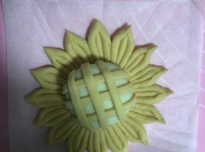 18.将包好的奶黄包封口向下，放入花瓣中央，并将黄色面条均匀搭在奶黄包上，面条端部塞入面团下。