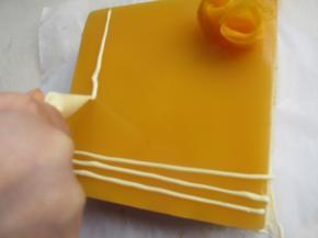 拿出慕斯，用吹风机把边上吹一圈，轻松脱模，白巧克力隔水融化，在慕斯上挤上几条装饰，摆上几朵芒果花。