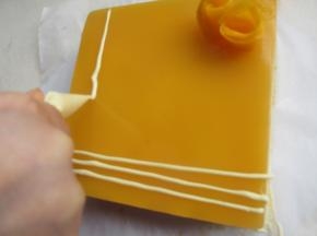 拿出慕斯，用吹风机把边上吹一圈，轻松脱模，白巧克力隔水融化，在慕斯上挤上几条装饰，摆上几朵芒果花。