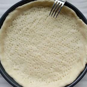 将面团排气，松弛15分钟，烤盘刷一层油，将面团擀成比披萨盘大一点的圆片，放在披萨盘中，用叉子叉出小孔