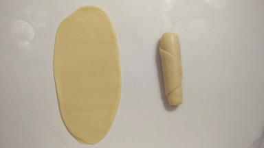 包好的面团收口朝上，用擀面杖擀成椭圆形，由下往上卷一起，这样就完成了第一次擀卷，全部面团都这样操作。