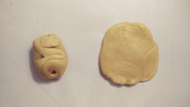 取一份白色面卷，从中间按压下去，将两头按到中间，用擀面杖擀成中间厚四周薄的圆形。