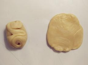 取一份白色面卷，从中间按压下去，将两头按到中间，用擀面杖擀成中间厚四周薄的圆形。