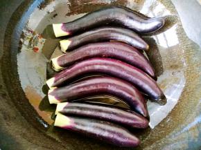 锅中倒油，量要比平时炒菜多一些。把每一根茄子上的水分擦干，依次摆放在锅中，开小火慢煎。