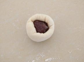 白色面团按扁，放上15克的豆沙，收口。