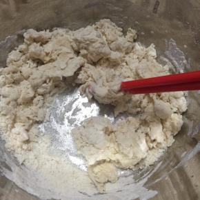 将披萨皮材料放入盆内，缓慢加入温水，用筷子不断搅拌成雪花状。