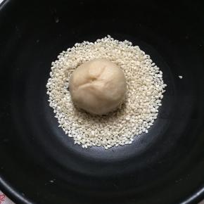 将滚圆的面团刷上一层薄薄的蛋清，然后粘上芝麻。