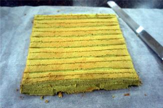 出炉后立即倒扣，撕走底部的硅胶垫，盖上一张新的吸油纸，放在烤架上冷却至温温的状态时倒扣过来，将蛋糕体的两端倾斜切去少许，以2cm的间隔划上浅刀痕，如图。