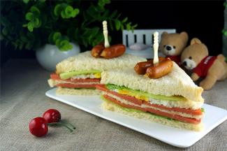 从底部到表层依次摆上吐司片、生菜、火腿片、芝士片、吐司片、火腿片、煎蛋、生菜、吐司片，然后用刀从对角将整体切成两份即可。