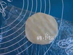 取一个冰皮面团，用手压扁或者用擀面杖擀扁。
如图我是用保鲜膜包着压的，这样可以解决很多人担心的粘手问题。